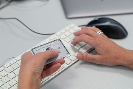 Hand håller i ett American Express medan den andra handen knappar in kortuppgifterna på ett tangentbord