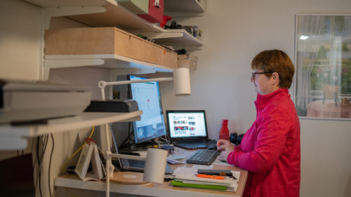 En kvinna står upp och arbetar vid sin dator på sitt hemmakontor.